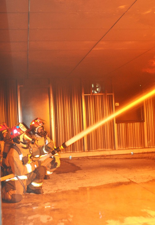 Three firefighters use a hose to douse fire in the ceiling of the college's new burn room during the Great Florida Fire School.