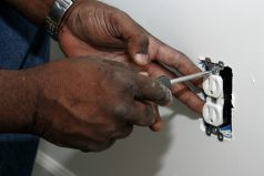 A pair of hands using a screwdriver to install an electrical outlet
