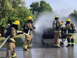 Fire Science students spraying water on a metal car form