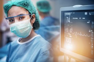 Team of doctors or surgeons with electrocardiogram monitor in hospital surgery operating emergency room showing patient heart rate, medical concept.