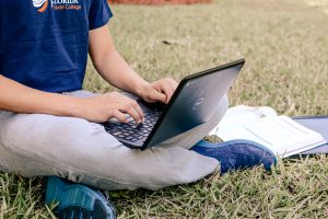 Male student sitting on the grass with a laptop in his lap.