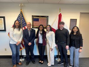 A group of six individuals standing in front of the American flag and the state flag of Florida.