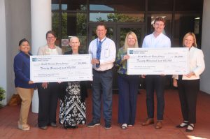 Group in front of the DeSoto Campus holding two big scholarship checks. 