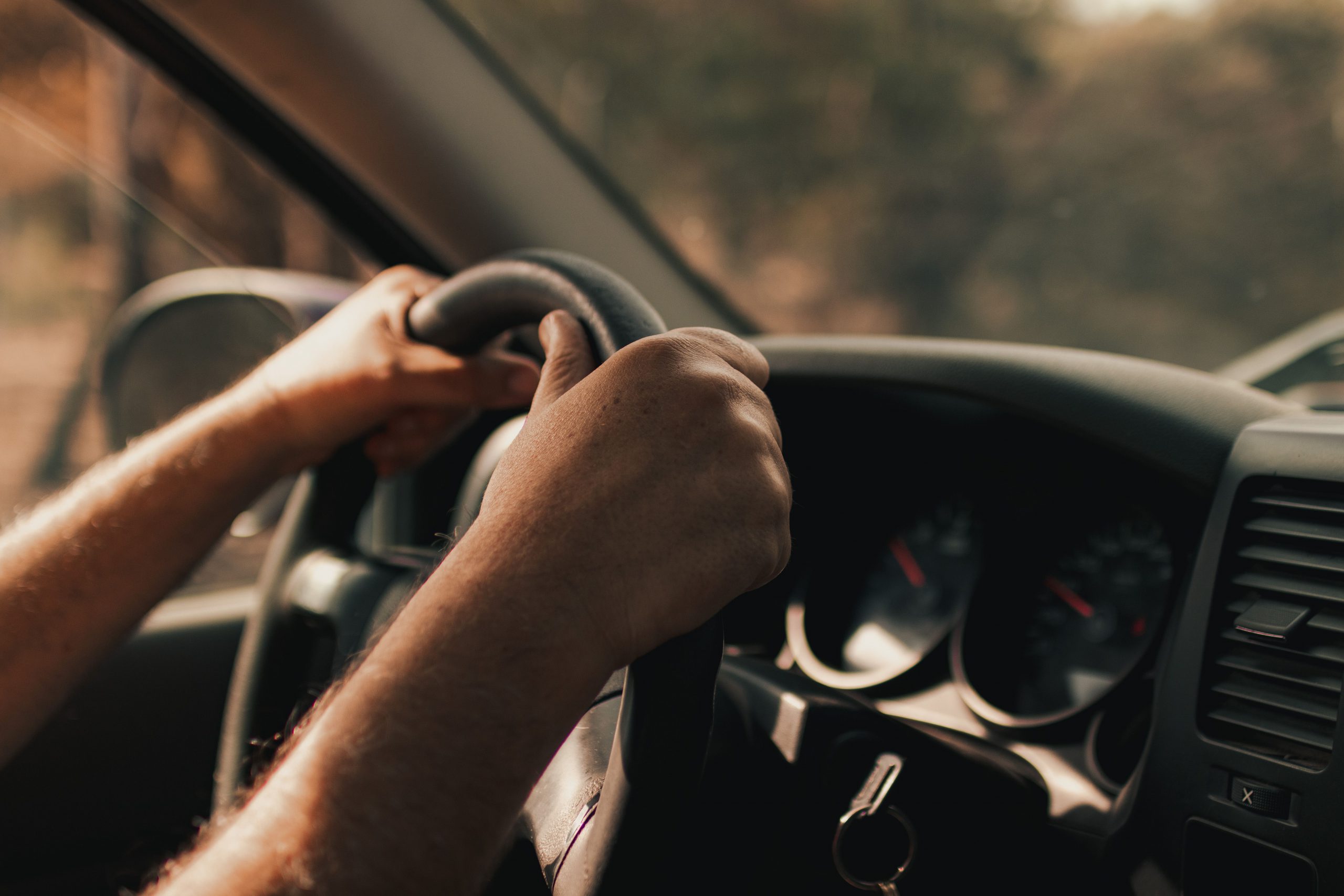 A drivers hands on the steering wheel with the dashboard in the background.